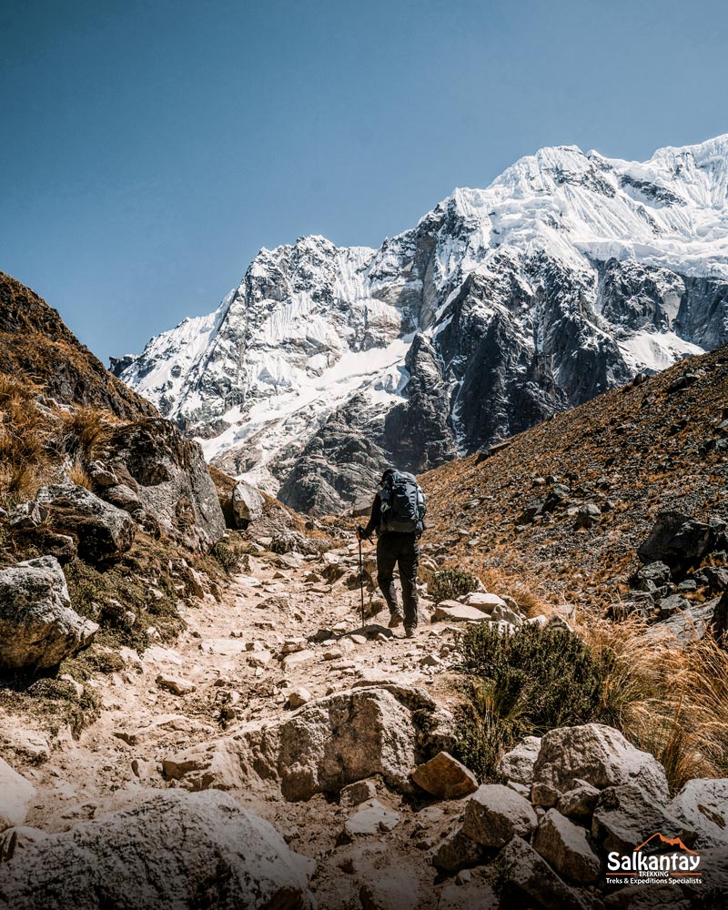 Turista caminhando em direção à passagem de Salkantay, ao lado da imensa montanha Salkantay.