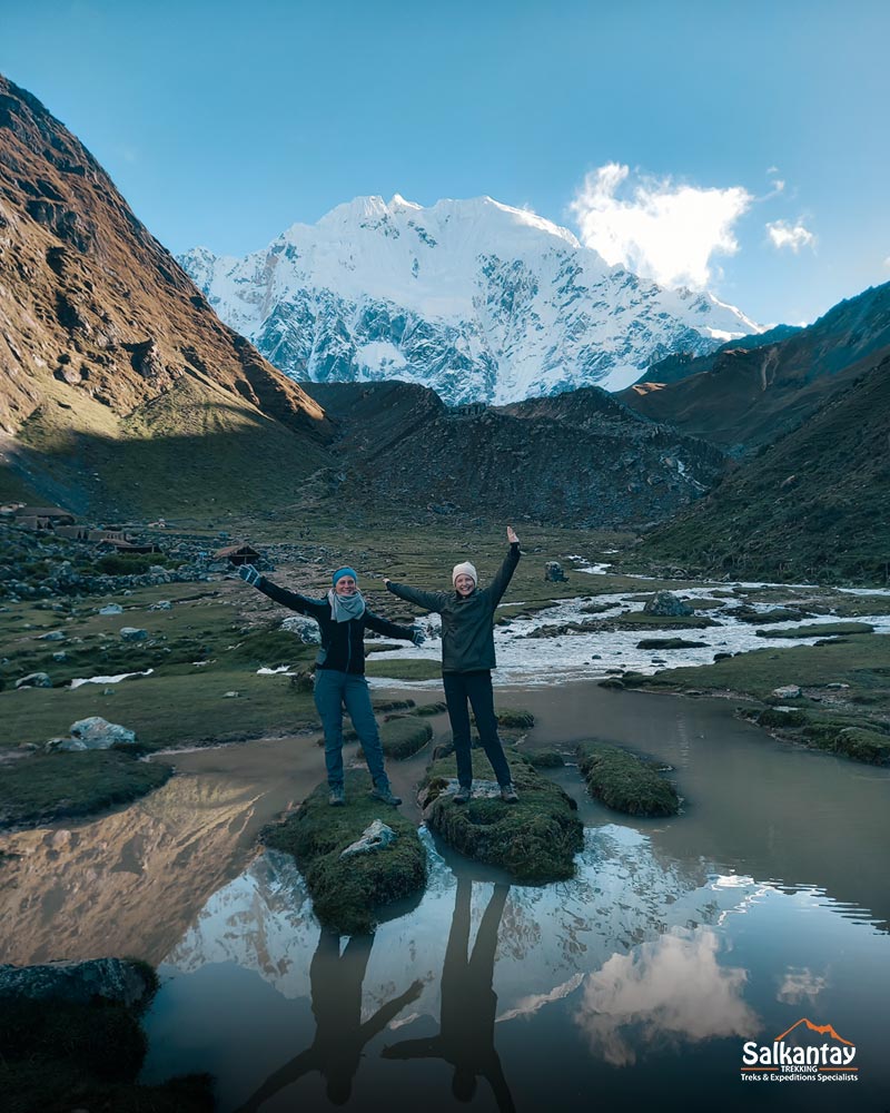 Dois turistas levantando as mãos em uma paisagem da ala de trilha de Salkantay.