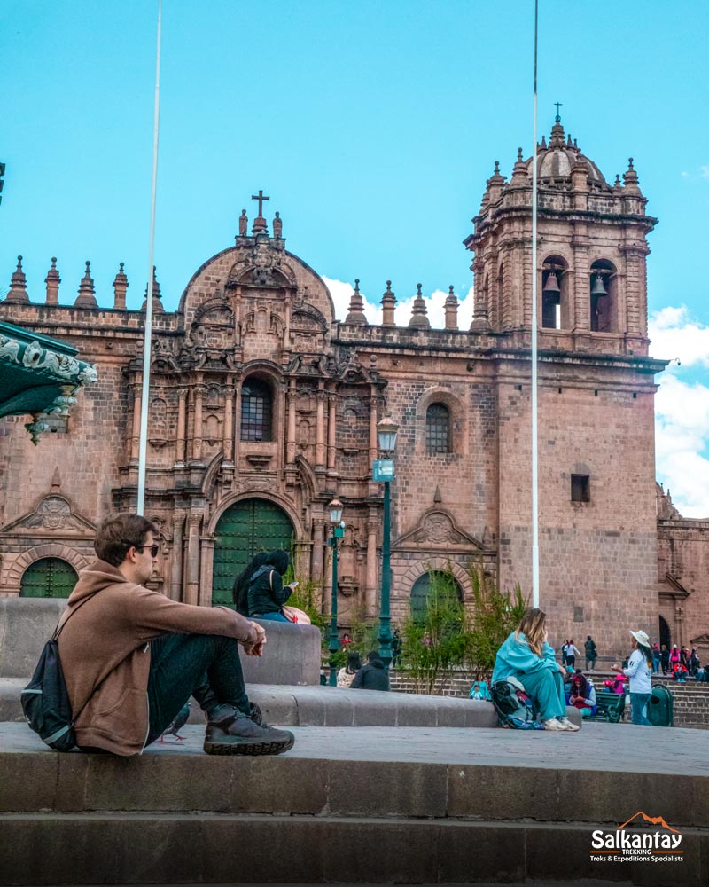 Turista sentado na praça principal de Cusco olhando para a catedral