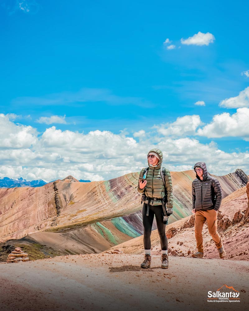 Dois turistas caminhando em Palccoyo com um cenário de montanhas coloridas