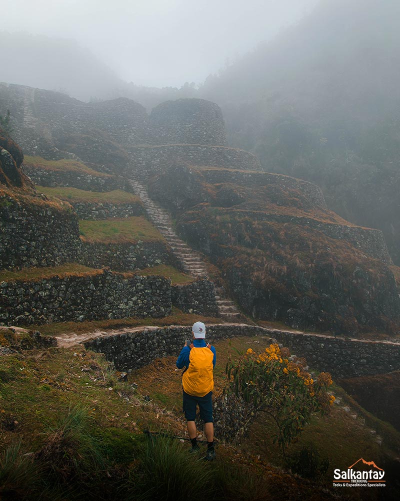 Turista con un mohair de color naranja en un yacimiento arqueológico del Camino Inca perdido en una inmensa niebla.